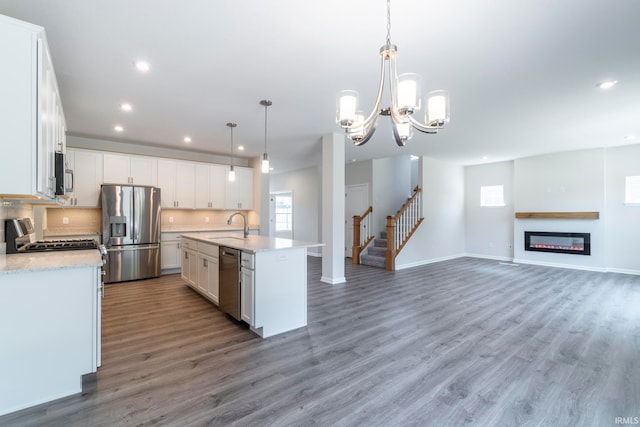 kitchen with decorative light fixtures, stainless steel appliances, dark hardwood / wood-style flooring, a notable chandelier, and an island with sink