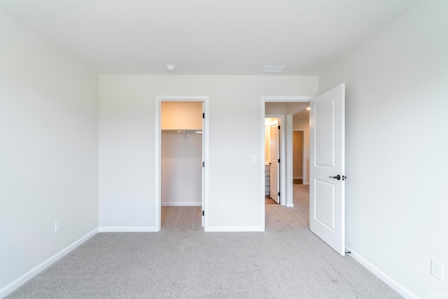 unfurnished bedroom with a walk in closet, a closet, and light carpet