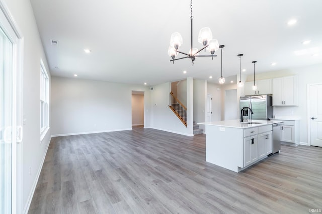 kitchen with light hardwood / wood-style flooring, decorative light fixtures, appliances with stainless steel finishes, a chandelier, and a center island with sink