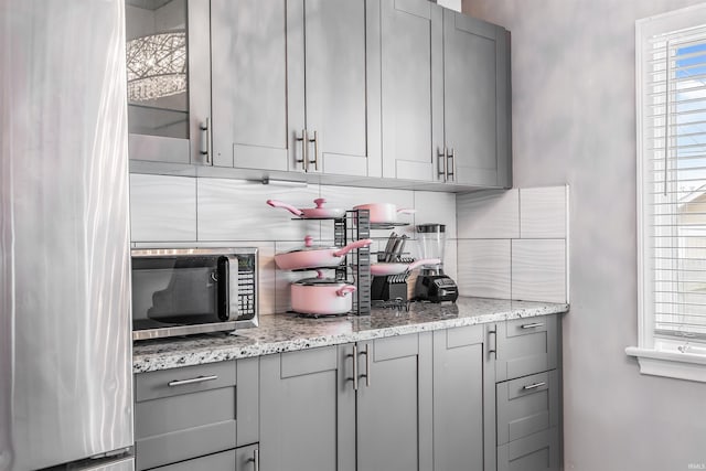 kitchen with gray cabinets, light stone counters, and backsplash