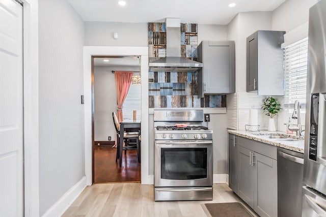 kitchen featuring wall chimney range hood, light stone countertops, stainless steel appliances, and light hardwood / wood-style flooring