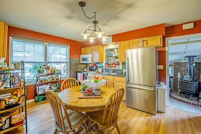 dining space featuring light wood-type flooring, a wood stove, a chandelier, sink, and a textured ceiling