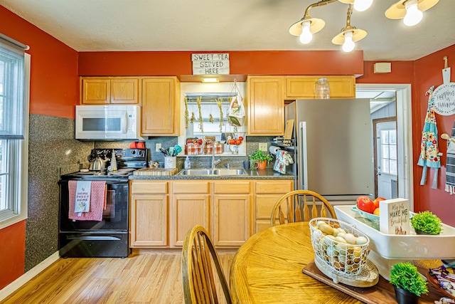 kitchen with stainless steel refrigerator, a notable chandelier, black range with electric cooktop, light hardwood / wood-style flooring, and sink