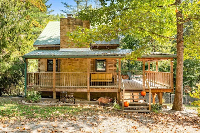 back of house with metal roof, a porch, and a chimney