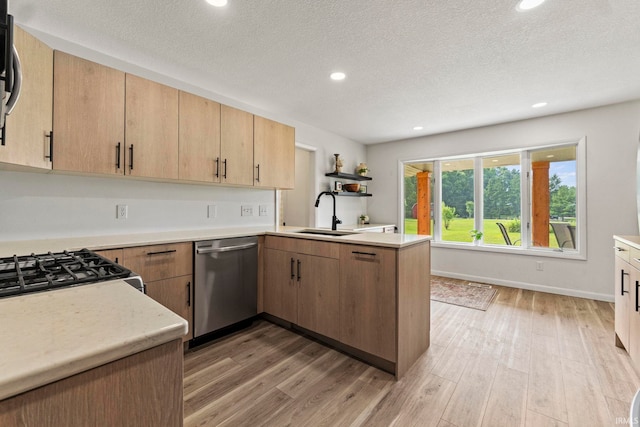 kitchen featuring a textured ceiling, wood-type flooring, appliances with stainless steel finishes, kitchen peninsula, and sink