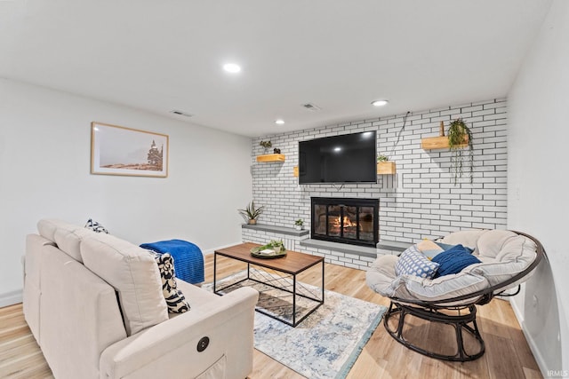 living room with brick wall, a brick fireplace, and light hardwood / wood-style flooring