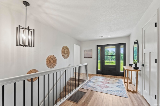 foyer entrance featuring a textured ceiling, a notable chandelier, and light hardwood / wood-style floors