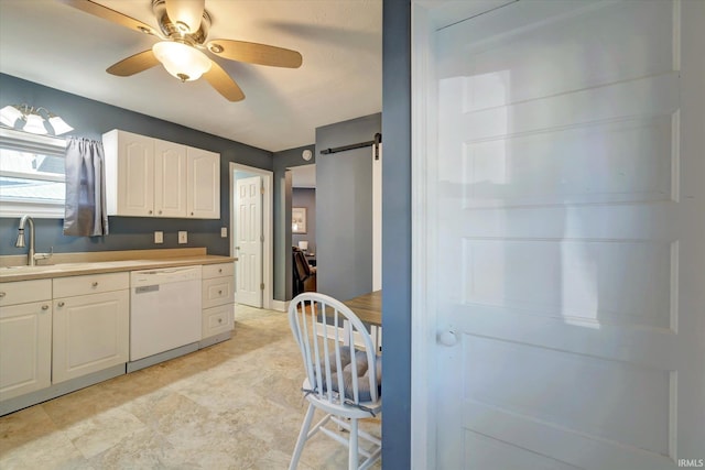 kitchen with white dishwasher, sink, a barn door, ceiling fan, and white cabinets