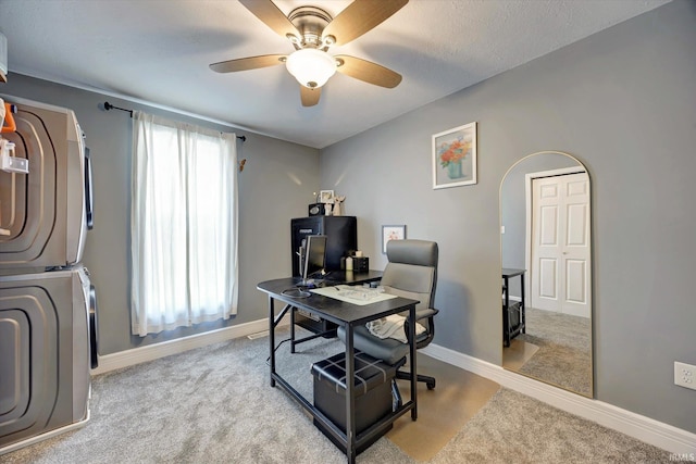 home office with light carpet, a textured ceiling, ceiling fan, and stacked washer and dryer