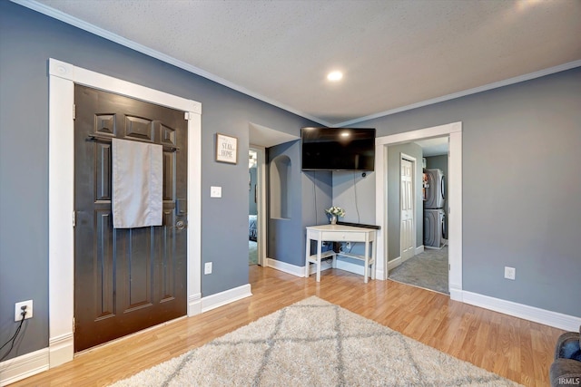 entrance foyer with ornamental molding, a textured ceiling, hardwood / wood-style floors, and stacked washing maching and dryer