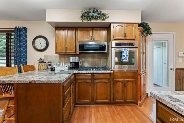 kitchen featuring light hardwood / wood-style flooring, backsplash, a kitchen bar, stainless steel appliances, and kitchen peninsula