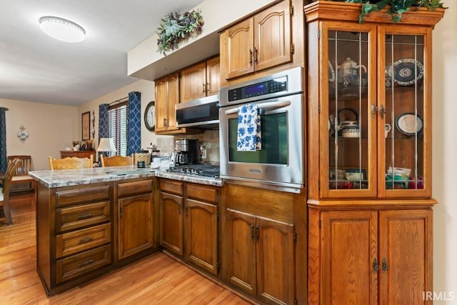 kitchen with light stone counters, kitchen peninsula, light wood-type flooring, and appliances with stainless steel finishes