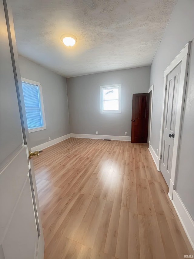 empty room with a textured ceiling and light hardwood / wood-style flooring