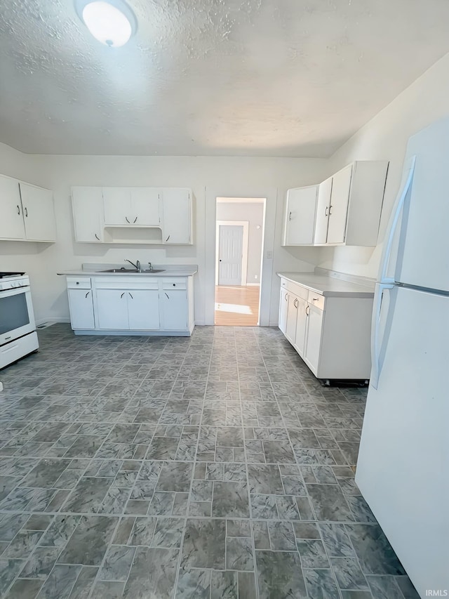 kitchen featuring white appliances, a textured ceiling, white cabinetry, and sink