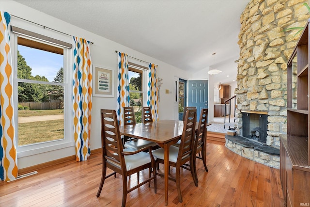 dining room with vaulted ceiling, a textured ceiling, light hardwood / wood-style flooring, and a stone fireplace