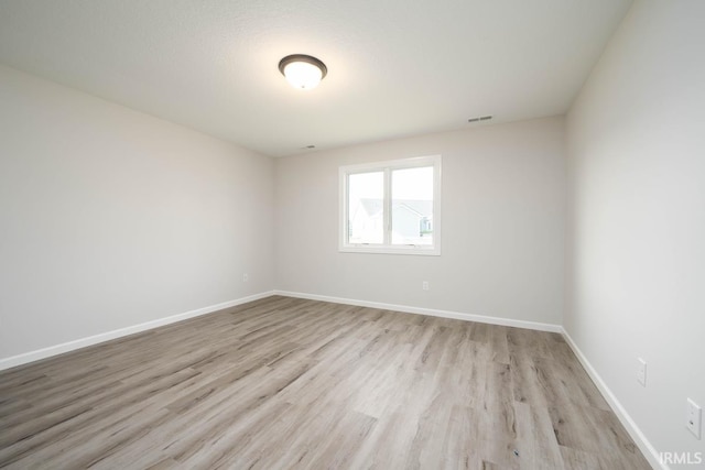 empty room featuring light wood-style floors, visible vents, and baseboards