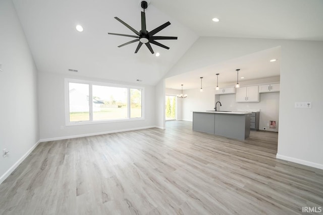 unfurnished living room featuring ceiling fan with notable chandelier, a sink, visible vents, baseboards, and light wood finished floors