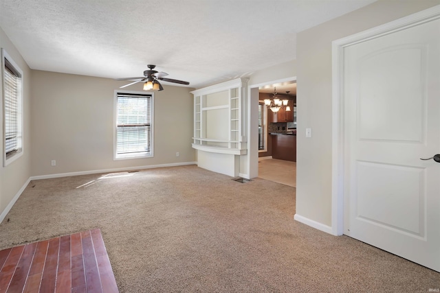 unfurnished room featuring a textured ceiling, light colored carpet, and ceiling fan with notable chandelier