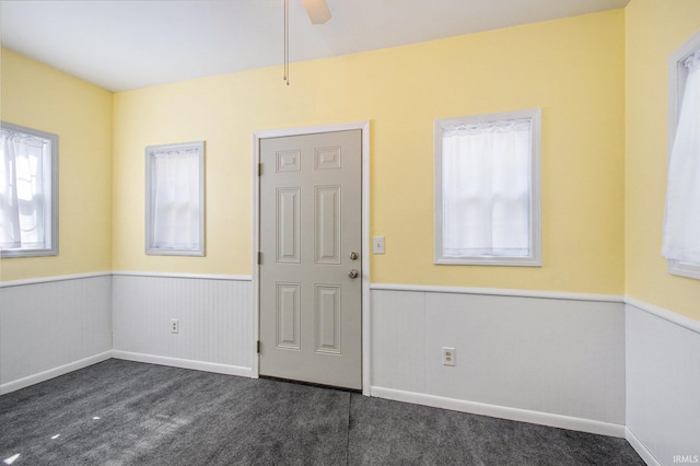 entryway with ceiling fan, plenty of natural light, and dark colored carpet