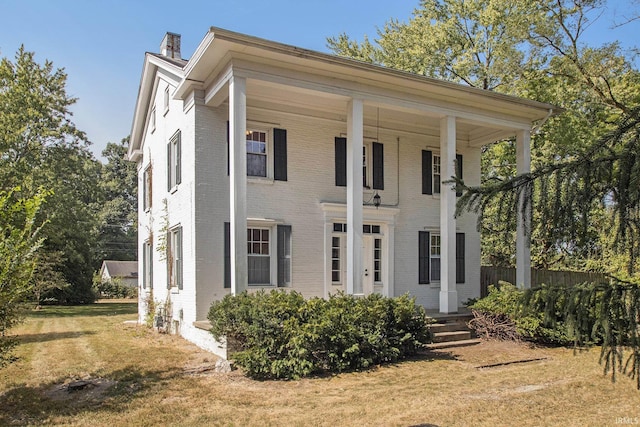 greek revival house with a front lawn, fence, brick siding, and a chimney