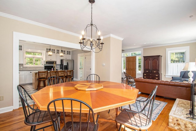 dining area with ornamental molding, an inviting chandelier, and light hardwood / wood-style floors