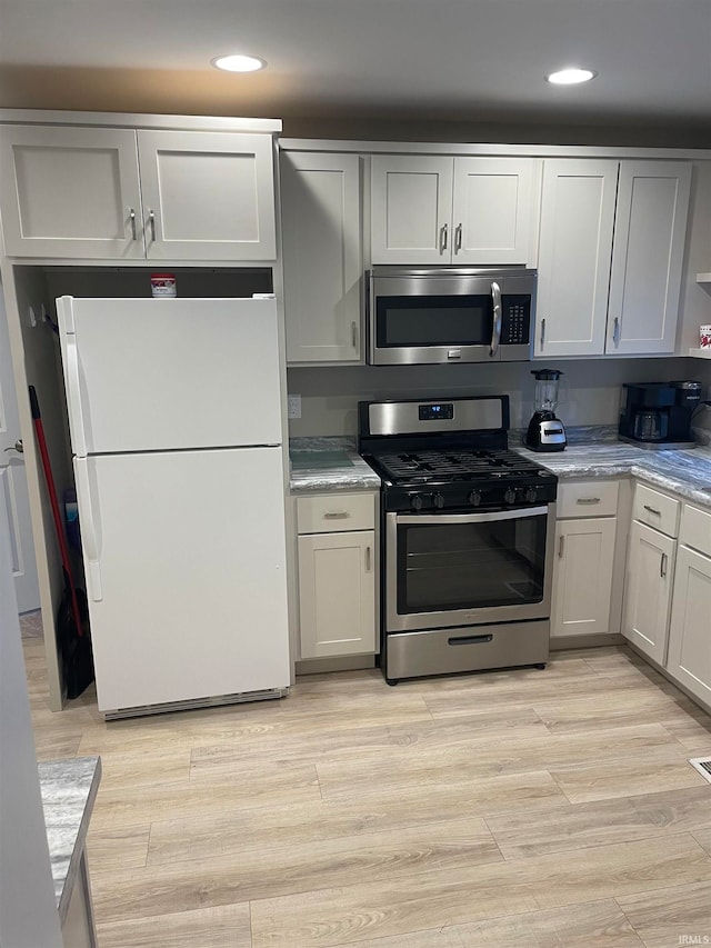 kitchen with light wood-type flooring, appliances with stainless steel finishes, and light stone countertops