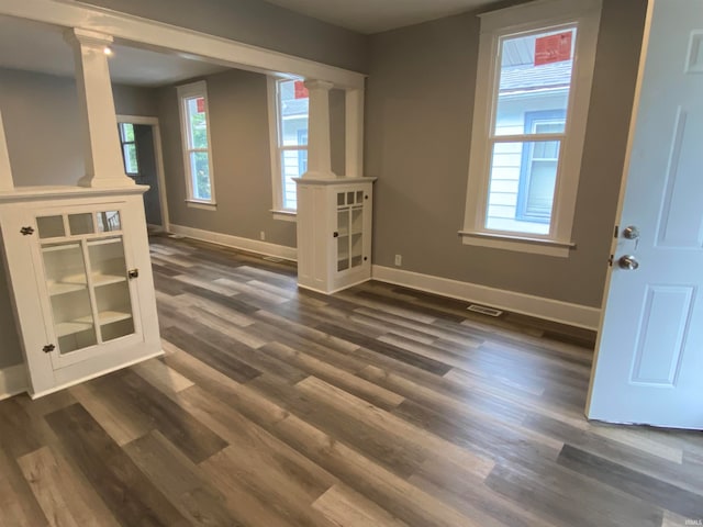 unfurnished room with visible vents, dark wood finished floors, decorative columns, and baseboards