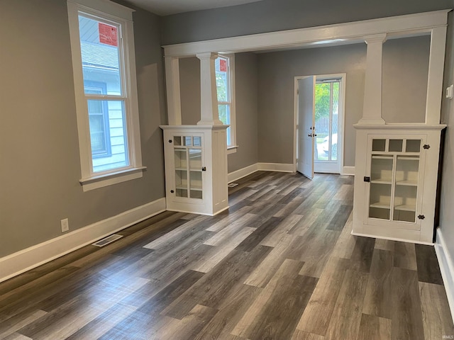 interior space with decorative columns, visible vents, baseboards, and dark wood-type flooring