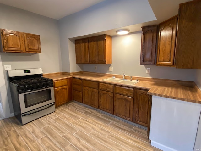 kitchen featuring wood finish floors, brown cabinetry, a sink, and gas stove