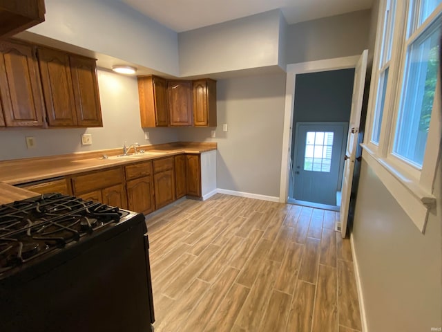 kitchen with a sink, light countertops, black range with gas stovetop, brown cabinets, and light wood finished floors