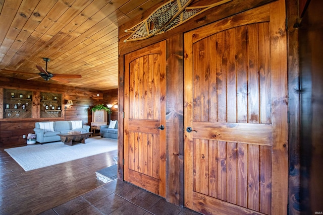 interior space with wood ceiling, ceiling fan, wood walls, and dark tile patterned floors