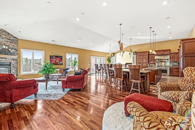 living room with vaulted ceiling, wood-type flooring, and a stone fireplace