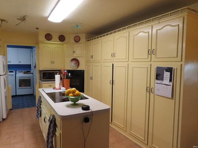 kitchen featuring light tile patterned floors, washing machine and clothes dryer, a kitchen island, cream cabinets, and black oven