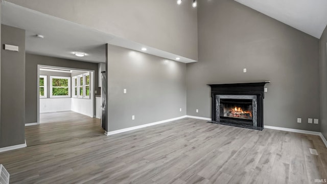 unfurnished living room featuring high vaulted ceiling, light wood-type flooring, and a fireplace