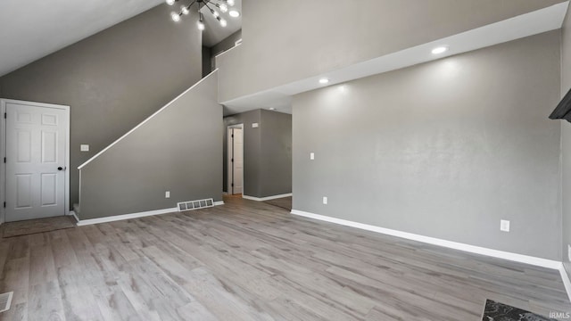 unfurnished living room with high vaulted ceiling, an inviting chandelier, and light hardwood / wood-style floors