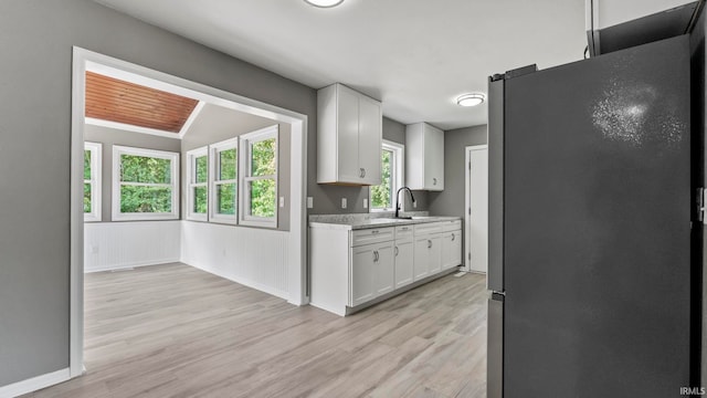 kitchen with stainless steel fridge, light wood-type flooring, white cabinetry, and light stone countertops