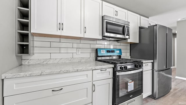 kitchen with light wood-type flooring, white cabinetry, stainless steel appliances, and light stone countertops