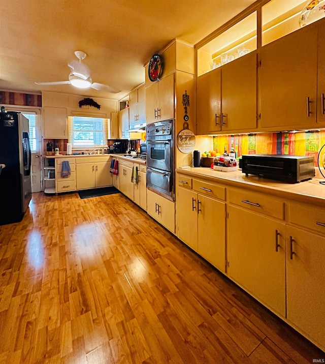 kitchen featuring stainless steel fridge with ice dispenser, light wood-type flooring, ceiling fan, and black oven