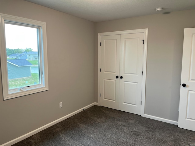 unfurnished bedroom with a textured ceiling, dark colored carpet, and a closet