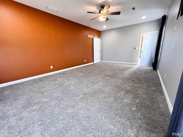 spare room with ceiling fan, a barn door, and carpet flooring