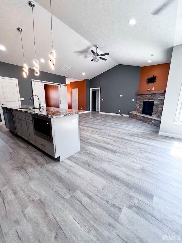 kitchen featuring pendant lighting, a stone fireplace, lofted ceiling, ceiling fan, and light stone counters