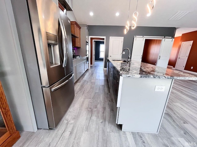 kitchen featuring a barn door, decorative light fixtures, stainless steel appliances, sink, and a center island with sink