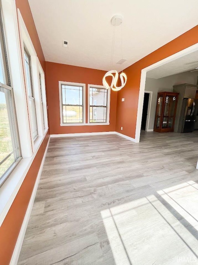 unfurnished dining area with light wood-type flooring and a notable chandelier