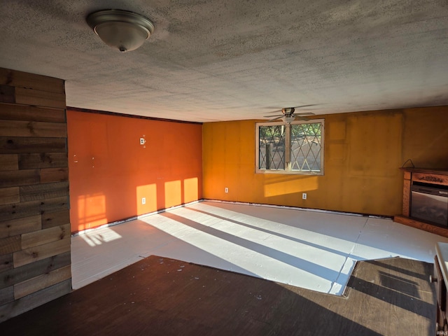 interior space featuring ceiling fan, a fireplace, wooden walls, and a textured ceiling