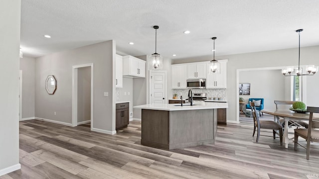 kitchen with pendant lighting, stainless steel appliances, light hardwood / wood-style floors, and a kitchen island with sink