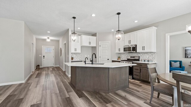 kitchen featuring stainless steel appliances, wood-type flooring, an island with sink, sink, and white cabinets