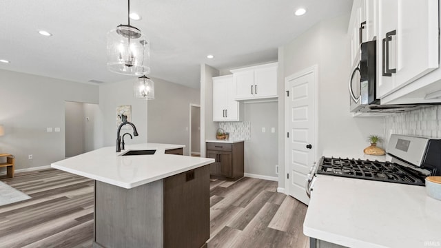 kitchen featuring white range with gas cooktop, a center island with sink, hanging light fixtures, sink, and white cabinetry