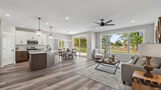 living room featuring ceiling fan with notable chandelier, a textured ceiling, hardwood / wood-style flooring, and sink