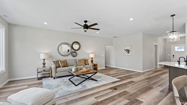 living room featuring ceiling fan with notable chandelier, a textured ceiling, light hardwood / wood-style flooring, and sink