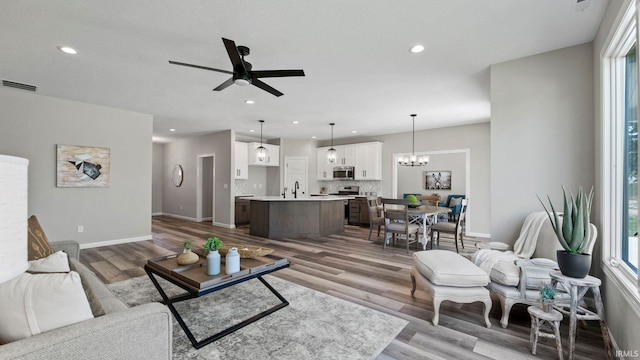 living room featuring ceiling fan with notable chandelier, hardwood / wood-style flooring, a healthy amount of sunlight, and sink